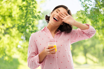 people and morning concept - happy yawning sleepy young woman in pajama with glass of orange juice over green natural background