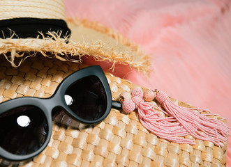 Woman clothes and accessories. Earrings, fragment of a straw bag, straw hat, black trendy sunglasses and fragment of a colorful dress