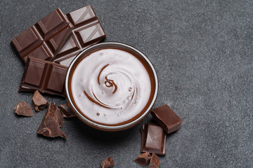 Melted chocolate or Hazelnut spread in glass bowl and chocolate pieces on dark concrete background