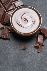Melted chocolate or Hazelnut spread in glass bowl and chocolate pieces on dark concrete background