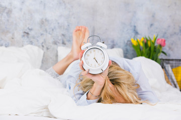 blonde, pretty young woman doesn't like to get up in the morning and hates her ringing alarm clock...