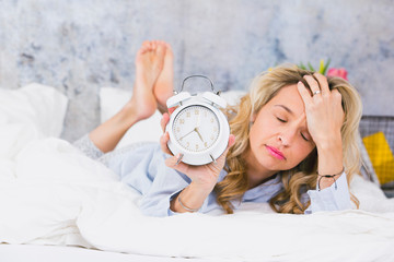 blonde, pretty young woman doesn't like to get up in the morning and hates her ringing alarm clock...