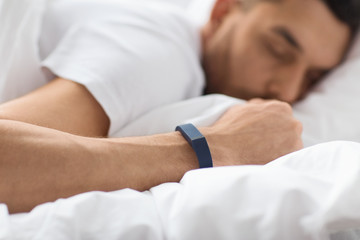 people, technology and rest concept - close up of man with activity tracker sleeping in bed
