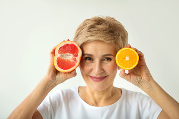 beautiful elderly woman in white t-shirt with orange and grape-fruit in hands on white background
