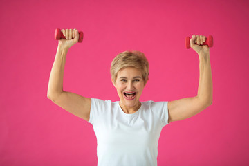 beautiful elderly woman in white t-shirt goes in for sports with dumbbells on a pink background