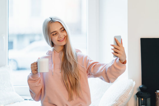 Carefree Girl Making Selfie With A Cup Of Coffee While Standing Near The Window At Home