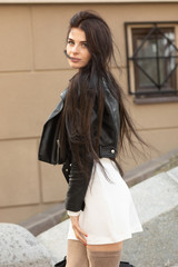 Fototapeta premium Young beautiful fashionable brunette woman in black leather jacket posing outdoors against urban style background
