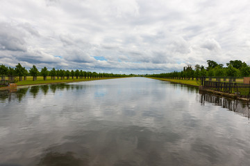 Still water canal near Hampton Court, England, with reflections from cloudy sky