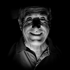 Portrait of smiling old caucasian man. Black and white shot, low-key lighting. Isolated on black.