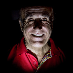 Portrait of smiling old caucasian man. Low-key lighting. Isolated on black.