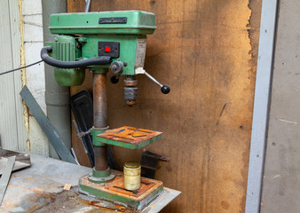 Old vertical green drilling machine with a big red power button and rust on the iron elements in an industrial production workshop. Tool for metal processing.