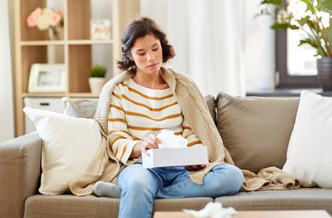 healthcare, cold, hygiene and people concept - sick woman in blanket taking paper tissue from box at home