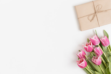 Bouquet of pink tulips and a gift on a white table. Flat lay with blank copy space.