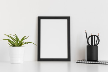 Black frame mockup with a succulent plant and workspace accessories on a white table. Portrait orientation.