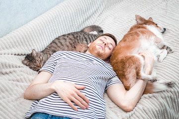 young man, a cat and a dog all sleep together on a bed.