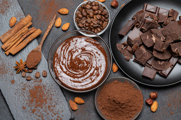 Melted chocolate or Hazelnut spread in glass bowl and chocolate pieces on dark concrete background