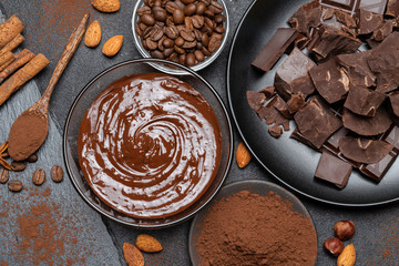 Melted chocolate or Hazelnut spread in glass bowl and chocolate pieces on dark concrete background