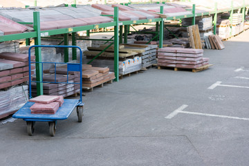 Fototapeta na wymiar Store building materials and street tiles. Display of decorative paving stones and road bricks at a stoneyard shop organized on display pallets for sale stored on wooden shelves outdoors
