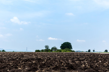 Plowed field in spring time with blue sky. Plowed ground, with brown stones and loose soil . Tractor plowing farm field in preparation for spring planting. Agriculture field ready for sowing seed.