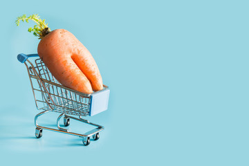 Grocery trolley with ugly carrot on blue. Space for text.