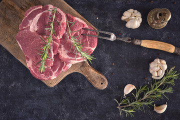 Raw meat steak on dark background and chopping board. Copy space text concept. Fresh rosemary and garlic.