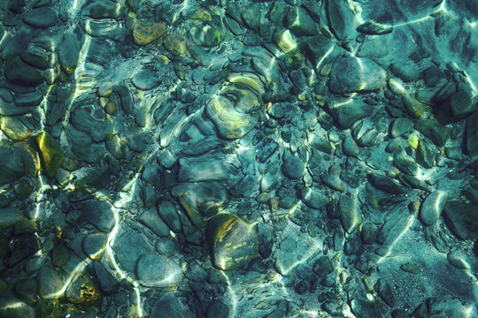 Beautiful shining colorful pebbles under clear turquoise water, background or texture