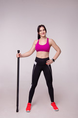 Beautiful muscular woman doing exercise with gymnastic stick on a gray background