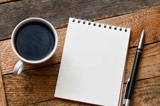 coffee cup, blank notepad and pen on wooden background, top view 