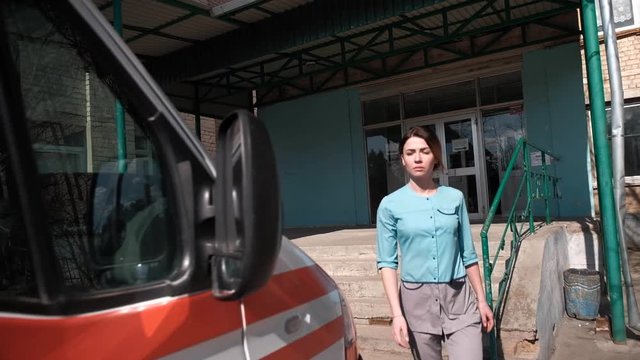 A young, graceful girl in medical special clothes, quickly leaves the building of the polyclinic to get into the emergency car and go to the call to the patient. The concept of the work of ambulance