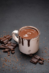 Cup of hot chocolate and pieces of chocolat on dark concrete background