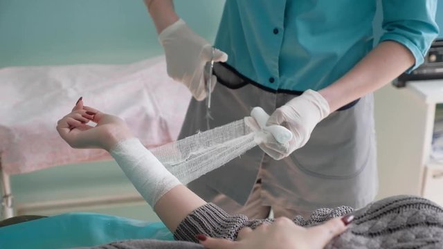 A nurse in the medical center diligently bandages the injured girl, she skillfully cuts a bandage with special scissors to fix the bandage