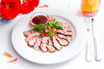 Tasty sliced roast duck breast with fresh vegetable salad and with cranberry sauce. Peking duck beast fillet on a plate with red wine and flowers