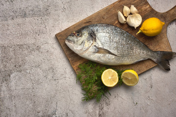 Fresh raw sea bream fish decorated with lemon slices, herbs and sea shells on background. Healthy food concept, top view, copy space. Dorado,