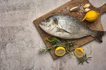 Fresh raw sea bream fish decorated with lemon slices, herbs and sea shells on background. Healthy food concept, top view, copy space. Dorado,