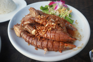 Fried crayfish with garlic decorated with purple orchid on a white ceramic dish put on leather floor the grid pattern.