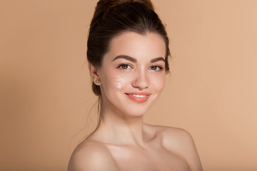 Beautiful face portrait of young woman with cosmetic cream on a cheek. Skin care and health concept.