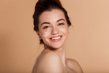 Beautiful face portrait of young smiling woman with cosmetic cream on a cheek. Skin care and health concept.
