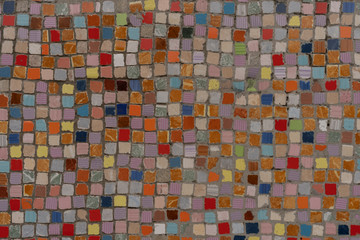 Closeup of multicoloured small square mosaic tiles evenly distributed to pattern mostly in hues of red.