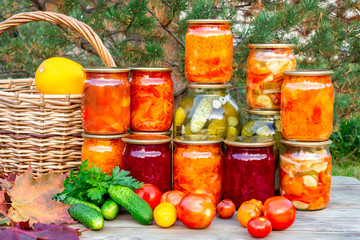 Several homemade jars of canned vegetables and fresh vegetables on a wooden table - image