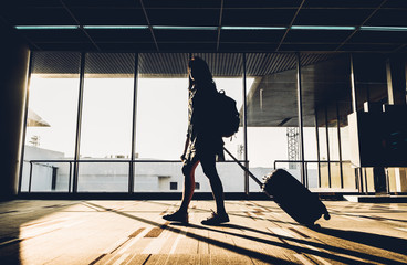 Silhouette of young girl walking with luggage walking at airport terminal window at sunrise time,travel concept,journey lifestyle
