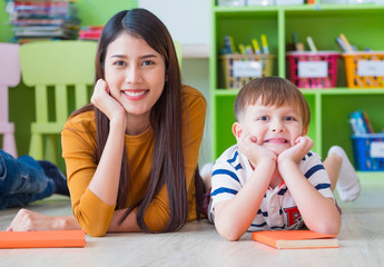 Kid and teacher looking at camera and smile lying down at school library. floor.kindergarden...