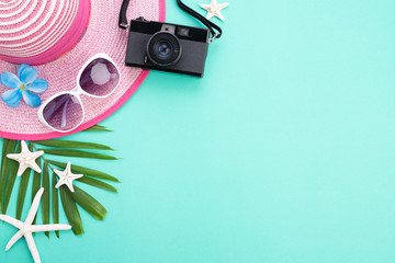 Beach accessories retro film camera, sunglasses, flip flop starfish beach hat and sea shell on green paper background for summer holiday and vacation concept.