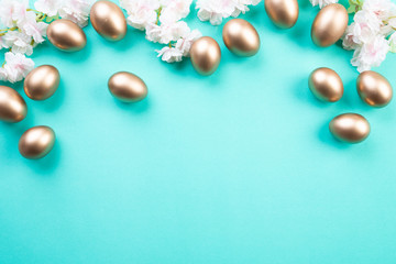 Happy easter! Row of golden Easter eggs with white and pink flower on green pastel background.