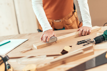 Female carpenter manually sanding wooden plank