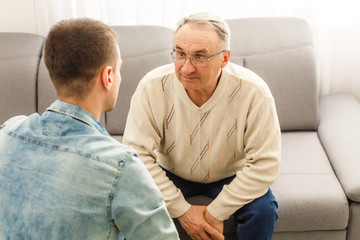 Young man sitting on a sofa smiling and talking with his grandfather