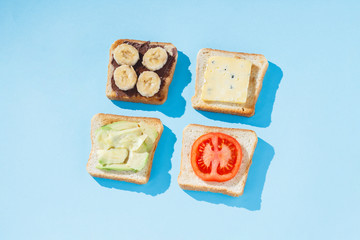 Sandwiches with cheese, tomato, banana and avocado on a blue background. Concept of healthy eating, breakfast at the hotel, diet. Natural lighting, hard light. Flat lay, top view.