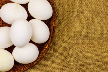 White chicken eggs in wicker basket on sackcloth background
