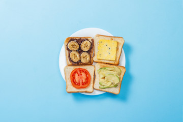 Sandwiches with cheese, tomato, banana and avocado on a white plate, blue background. Concept of healthy eating, breakfast at the hotel, diet. Natural lighting, hard light. Flat lay, top view.