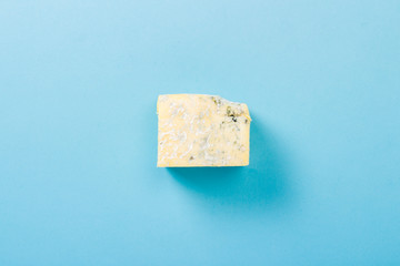 A piece of blue cheese on a blue background. Minimalism. Flat lay, top view.