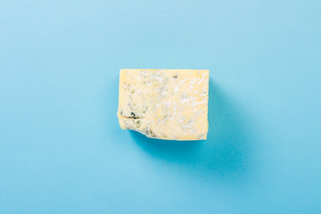 A piece of blue cheese on a blue background. Minimalism. Flat lay, top view.